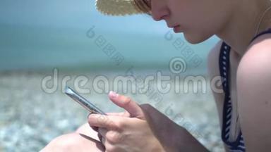 漂亮的年轻女人在海边使用智能手机。 穿着复古帽子和<strong>蓝白</strong>条纹泳衣的女孩