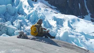 带着黄色背包的游客看着一座美丽的冰川。 把石头扔下去