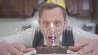 一个戴着生日帽的滑稽年轻人坐在厨房里的一个小巧克力蛋糕前面的模糊肖像。 这就是