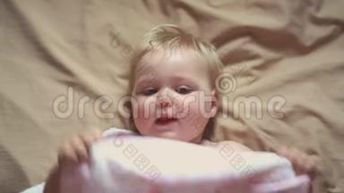 可爱可爱的宝贝女孩躺在床上玩毛巾的肖像。 幼儿宝宝微笑，在家感到快乐..