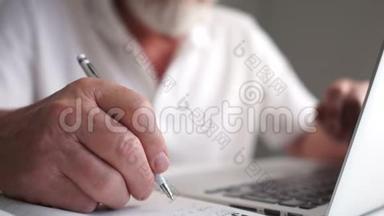 特写镜头，一位老人在<strong>用笔</strong>记本电脑工作时，<strong>用笔</strong>在笔记本上做笔记。 一个成熟的商人