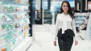 美丽的年轻微笑的女人走在化妆品店的销售区