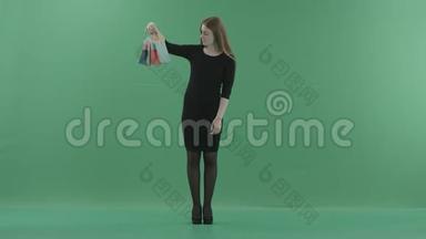 漂亮的笑女人穿着黑色的<strong>小裙子</strong>在摆姿势和玩购物袋。 她站在