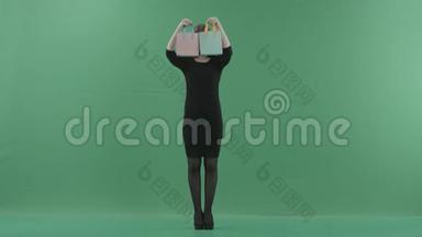 漂亮的笑女人穿着黑色的小裙子在摆姿势和玩购物袋。 她站在