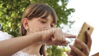 手里拿着手机的少女在传感器屏幕上滚动。 现代小玩意。 公园青少年活动