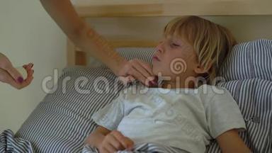 在床上生病的小男孩。 妈妈吻了吻他，用精油`男孩的胸部涂上药膏。 婴儿流感概念