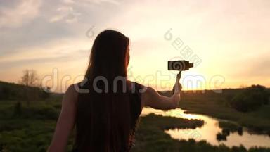 年轻的博客女孩在日落时用手机和万向节制作视频。
