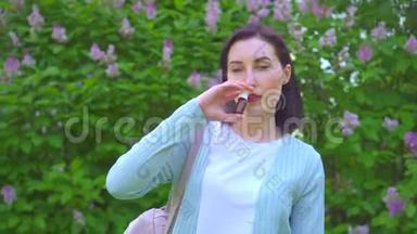 一位年轻女子在公园里开花植物的背景上用过敏鼻喷雾的肖像