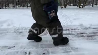 一个小孩子的脚在冬天的雪和柏油路上迈出我的第一步。 小宝宝学会走路.. 第一批