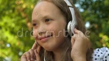 有趣的宝宝听音乐。 戴着耳机的快乐女孩在夏天的公园里听音乐和跳舞。 快关门。