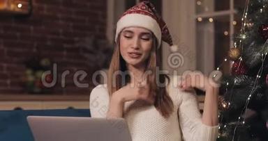 一位戴着圣诞帽、笑容满面的白种人女士坐在<strong>圣诞树</strong>旁舒适的家中的沙发上打着<strong>视频</strong>电话