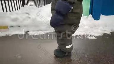 一个小孩子的脚在冬天的雪和柏油路上迈出我的第一步。 小宝宝学会走路.. 第一批