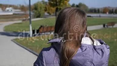 公园里的女孩。 穿着羽绒服的迷人女孩走在秋天的公园里，微笑着抚摸着她的头发