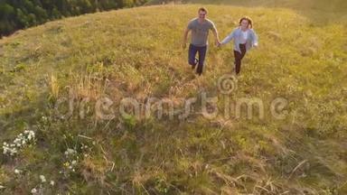 一对年轻夫妇在日落时愉快地穿过一片山地<strong>草地</strong>的<strong>航拍</strong>镜头。