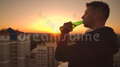 一个人喝着啤酒站在屋顶上沉思世界。 从高处看日落时的城市景色