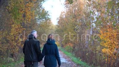 一个身材苗条，头发花白的男人戴着眼镜，一个身材苗条、漂亮、中年的女人走在秋天公园大道的下面