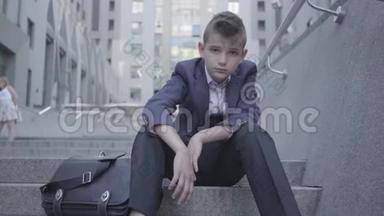 穿着西装的可爱男孩坐在街上的楼梯上。 这个男孩<strong>很累</strong>，只想成为一个