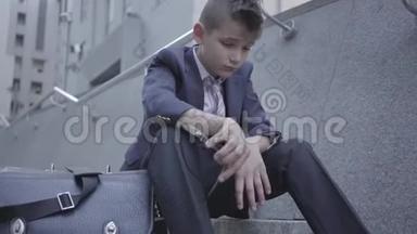 悲伤的衣冠楚楚的男孩坐在街上的楼梯上，靠近他的旧钱包。 3.那个男孩摘下眼镜，感到<strong>很累</strong>