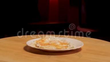 煎蛋放在盘子上，在黑暗的房间背景上的木板上旋转。 库存录像。 关上白色玻璃板