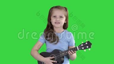 小女孩一边唱着小吉他，一边走向绿色屏幕上的相机，Chroma键。