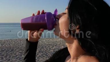 日出时，一个漂亮的黑发女孩在<strong>海洋</strong>背景上喝着运动<strong>瓶</strong>中的蛋白质奶昔。