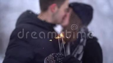 模糊的数字，年轻的男人和女人接吻的背景下，燃烧的火花在白雪覆盖的公园。 冬季