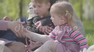 母亲在公园里系着可爱的金发小女儿的鞋，而其他母亲则在坐着拥抱她的小儿子