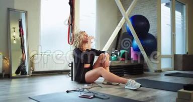 口渴的女士经<strong>过</strong>一次艰苦的健身房锻炼后，她坐在地板上喝点水和<strong>轮胎</strong>，度<strong>过</strong>了一段轻松的时光