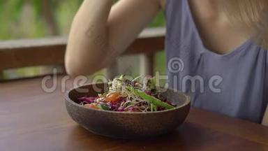 一个在热带咖啡馆里的年轻女人吃健康的素食沙拉。 素食概念