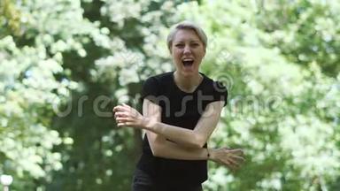 快乐的金发女人在闷热的公园里笑着举起双手