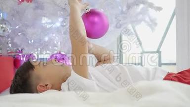 孩子躺在<strong>圣诞树</strong>下玩粉色球的<strong>视频</strong>。