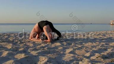 在<strong>海边</strong>或<strong>海边</strong>的沙滩上做<strong>瑜伽</strong>的健身女孩。 穿着黑色紧身衣的女孩练习和放松。 健康观念。