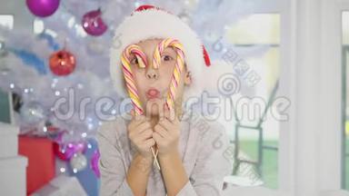 4k视频圣诞男孩坐在圣诞树附近，玩糖果，透过一根甘蔗心