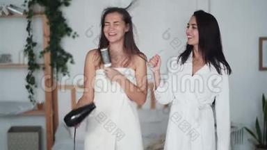 两位年轻女士穿着<strong>白色浴袍</strong>跳舞，带吹风机唱歌，吹干头发，开怀大笑