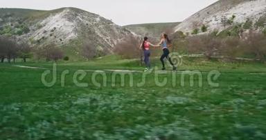 在一个完美的夏日里，两个女人穿过一片绿色的田野和山景，在大自然中锻炼身体。