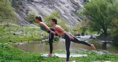 漂亮的两位身材匀称的女士在美丽的自然景观中一起练习瑜伽，她们伸展着河流