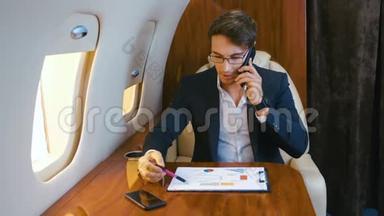 忙碌的商人在私人喷气式飞机上飞行时，处理文件和在手机上交谈。 飞机