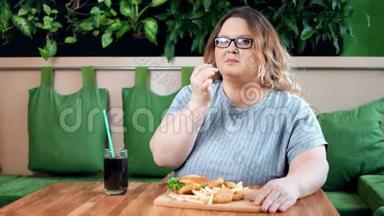快乐的胖女人在咖啡馆里吃着开胃的炸薯条、汉堡和金块，看着镜头