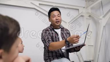韩国教师坐在桌子上的肖像，手里拿着笔记本电脑给学生上课。 小学学生