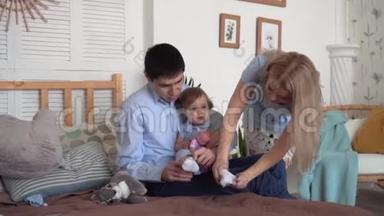 一家人在床上微笑，爸爸妈妈和他们的小女儿一起穿袜子