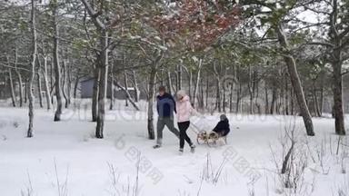 幸福的家庭在下雪的冬天滑雪。 父亲和母亲在下雪时和儿子拉雪橇绳索。 户外男孩雪橇
