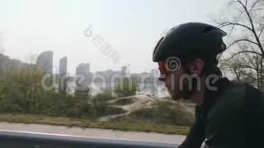 年轻的骑自行车的人，留着胡子，戴着太阳镜，戴着头盔，穿着黑色衣服骑自行车。特写侧视图。自行车概念。慢m