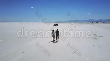 <strong>无人机</strong>跟着男人和女人牵着手，在<strong>大气</strong>的盐漠湖景观中间朝汽车跑去。