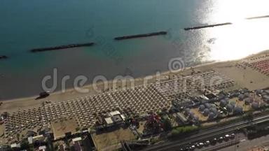 无人机在美丽的<strong>夏季</strong>意大利海岸上空盘旋，公共<strong>沙滩</strong>上有一排排椅子，阳光在水中反射。