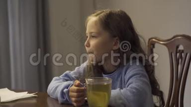 可爱的小<strong>女孩</strong>一边喝凉茶，一边坐在家里的桌子上。 在厨房里喝茶治<strong>感冒</strong>的孩子