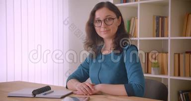 年轻漂亮的白种人女学生戴着眼镜，端着平板电脑看着镜头微笑的特写照片
