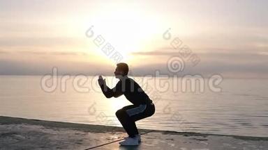 迷人的，运动的高个子穿着短裤在靠近大海的木地板上热身。 做仰卧起坐和跳跃