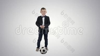 穿正式西装的男孩在梯度背景下踢足球。