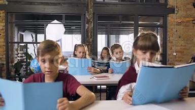 白人小学生坐在课桌前学习，在教室里看书。 教育和学生