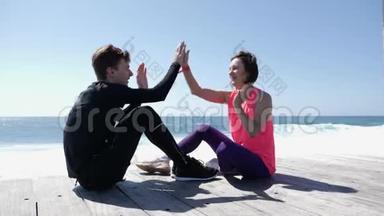 快乐的年轻男友和女友坐在海边玩击掌游戏。 波浪溅落在岩石上. 奴隶